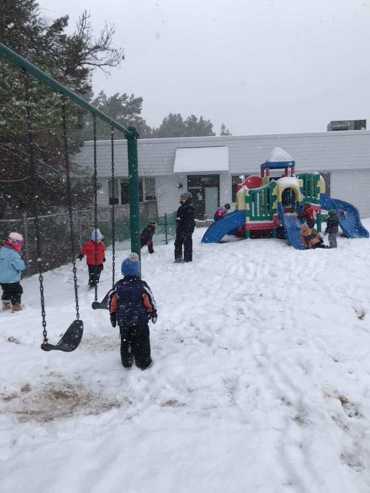 Children playing in a snowy playground with swings and a climbing structure