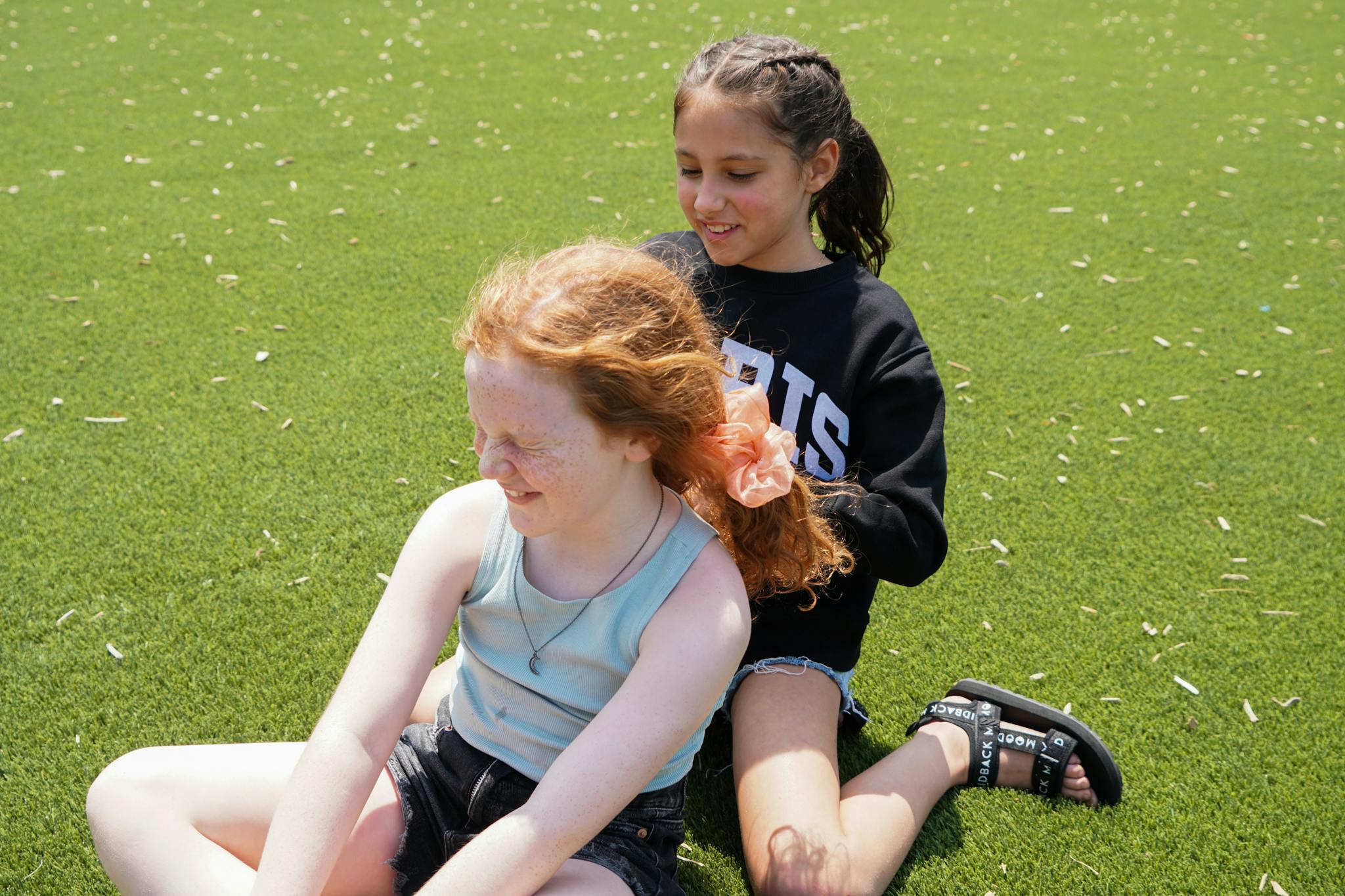 Teen braiding another child's hair on grass