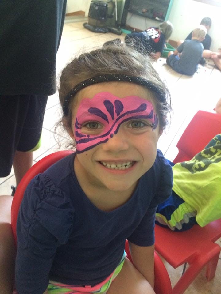 Child with pink and purple face paint on one side of face