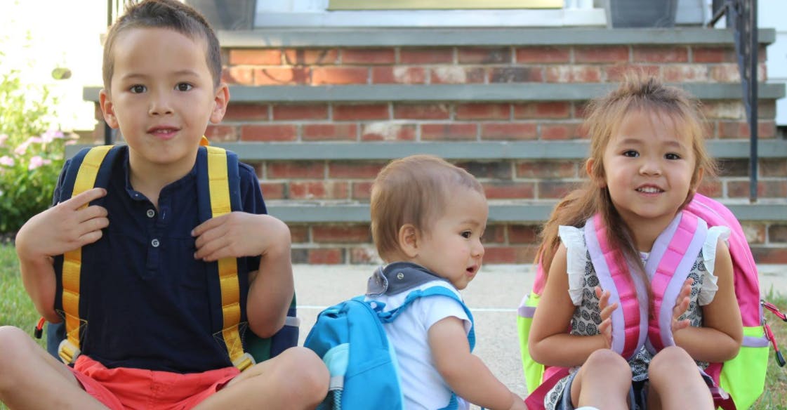 Three children wearing backpacks sitting outdoors
