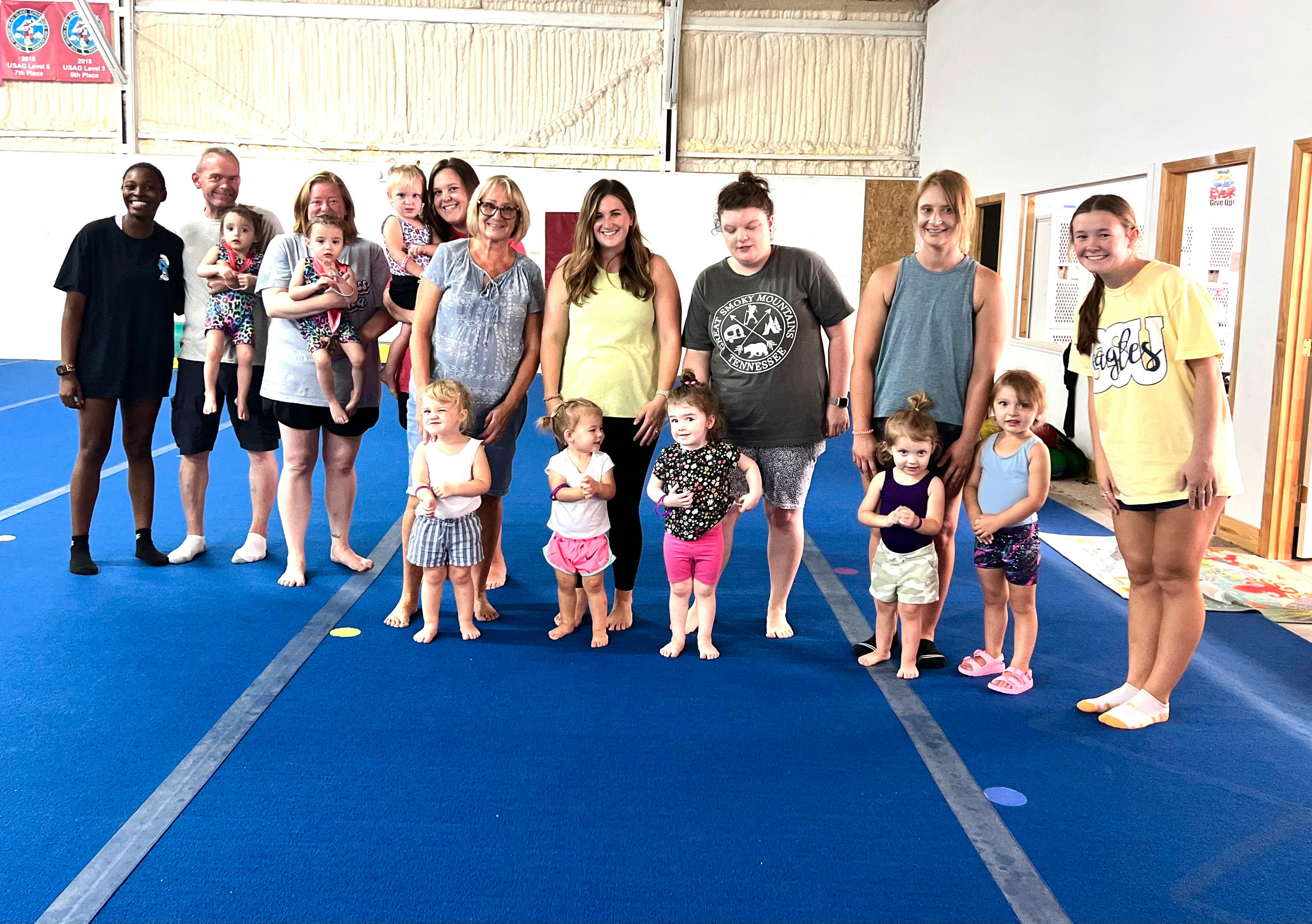 Group of adults and children standing on a blue mat