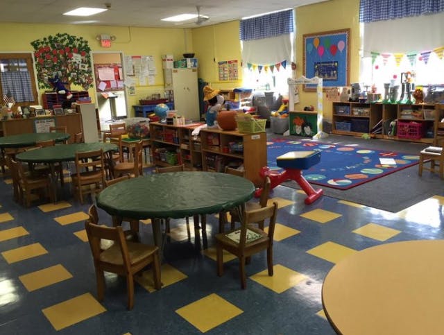 Classroom with small tables and chairs, colorful rug, and decorations