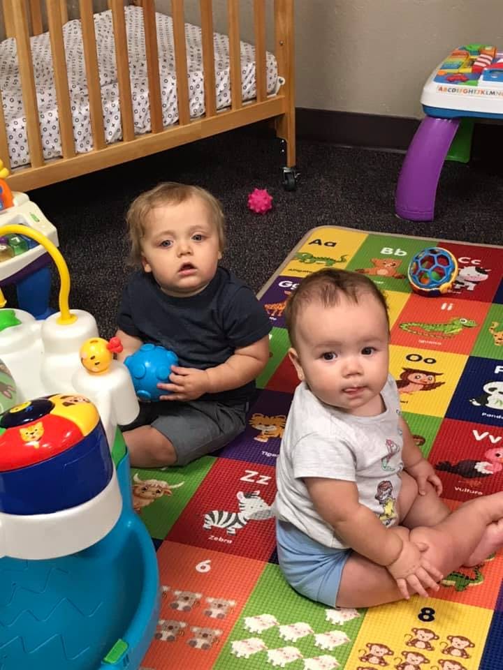 Two children sitting on a colorful playmat with toys