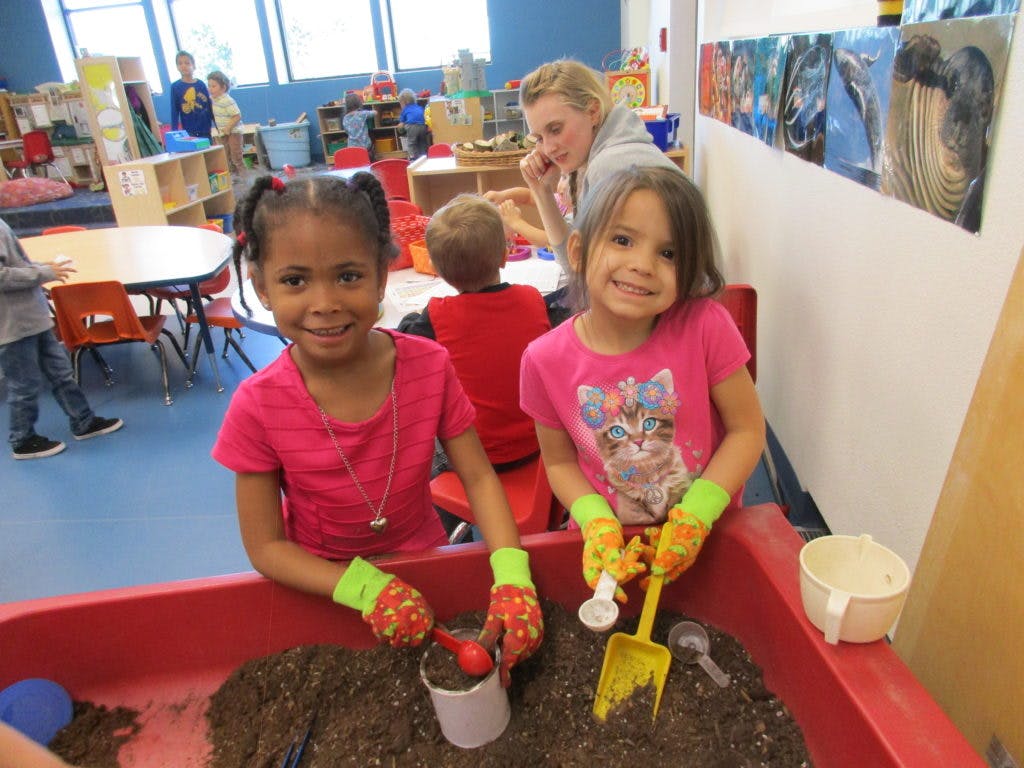Two children wearing gloves playing in a sand table