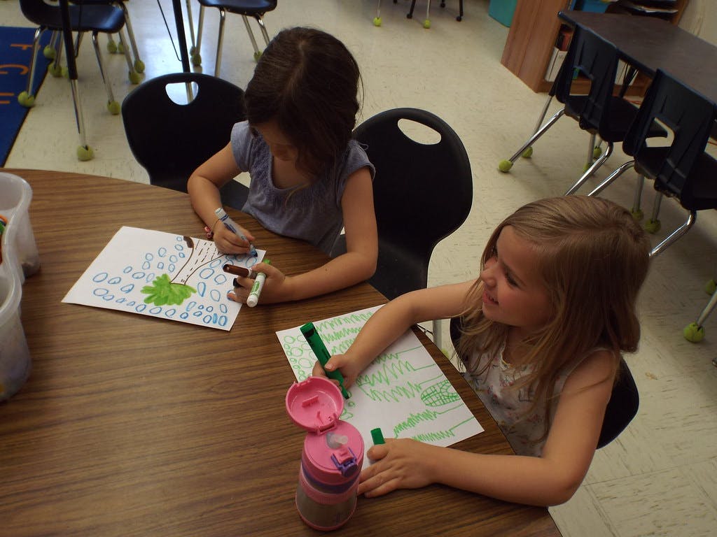 Two children drawing at a table in a classroom