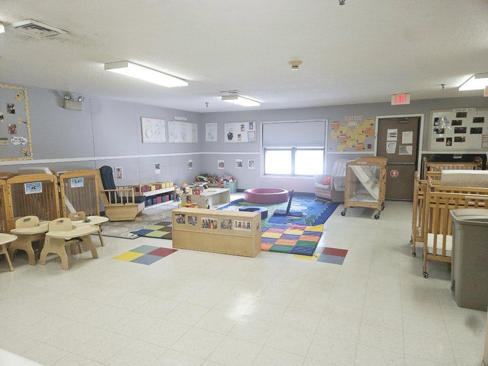 A childcare classroom with cribs, small chairs, and toys
