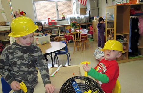 Two children wearing yellow hard hats playing in a classroom
