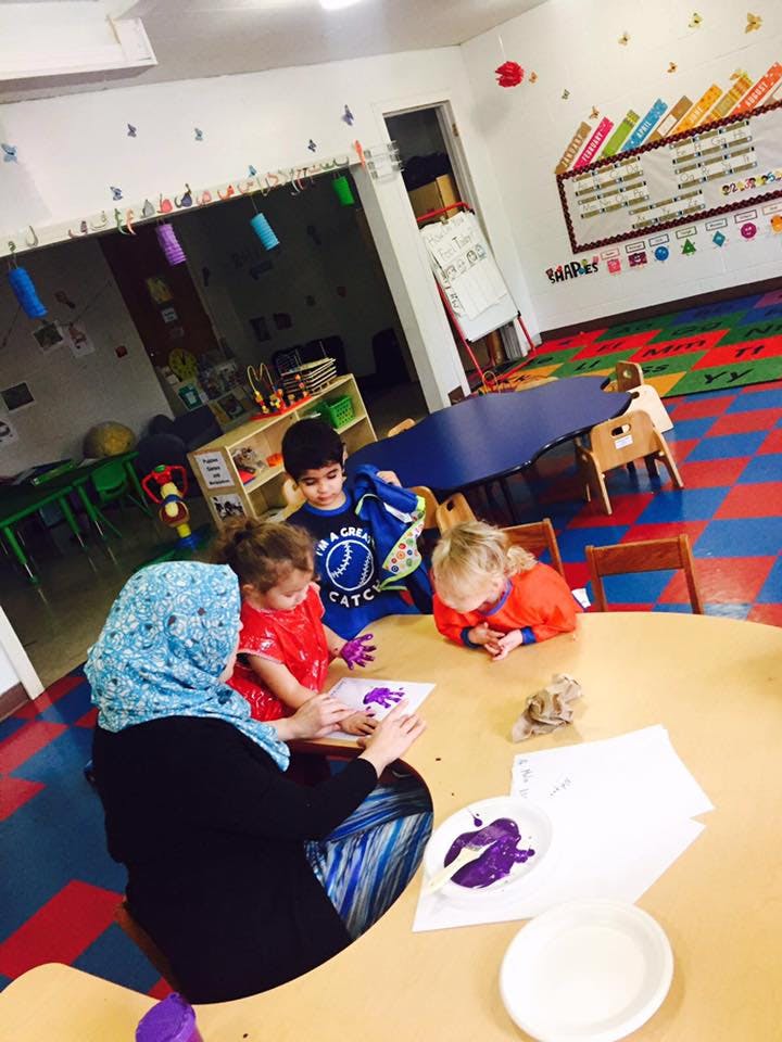 Person and children doing finger painting in a classroom
