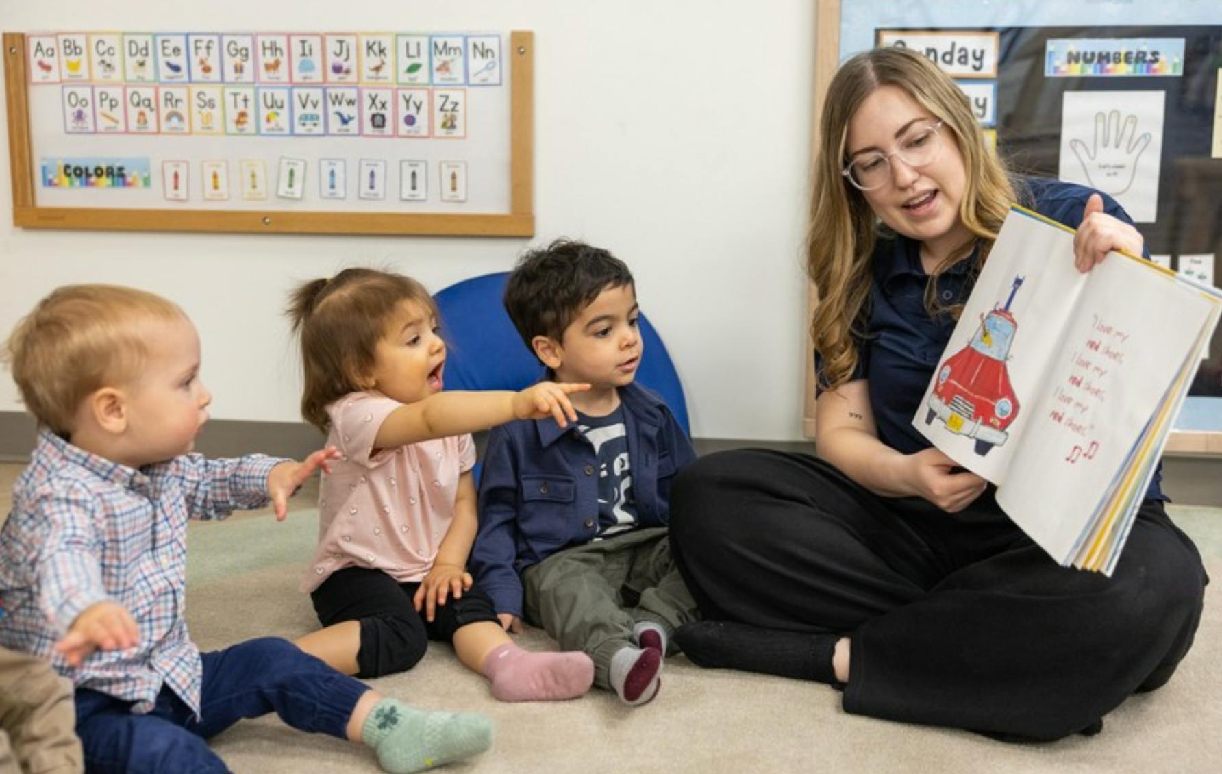Adult and three children sitting on floor, looking at a picture book