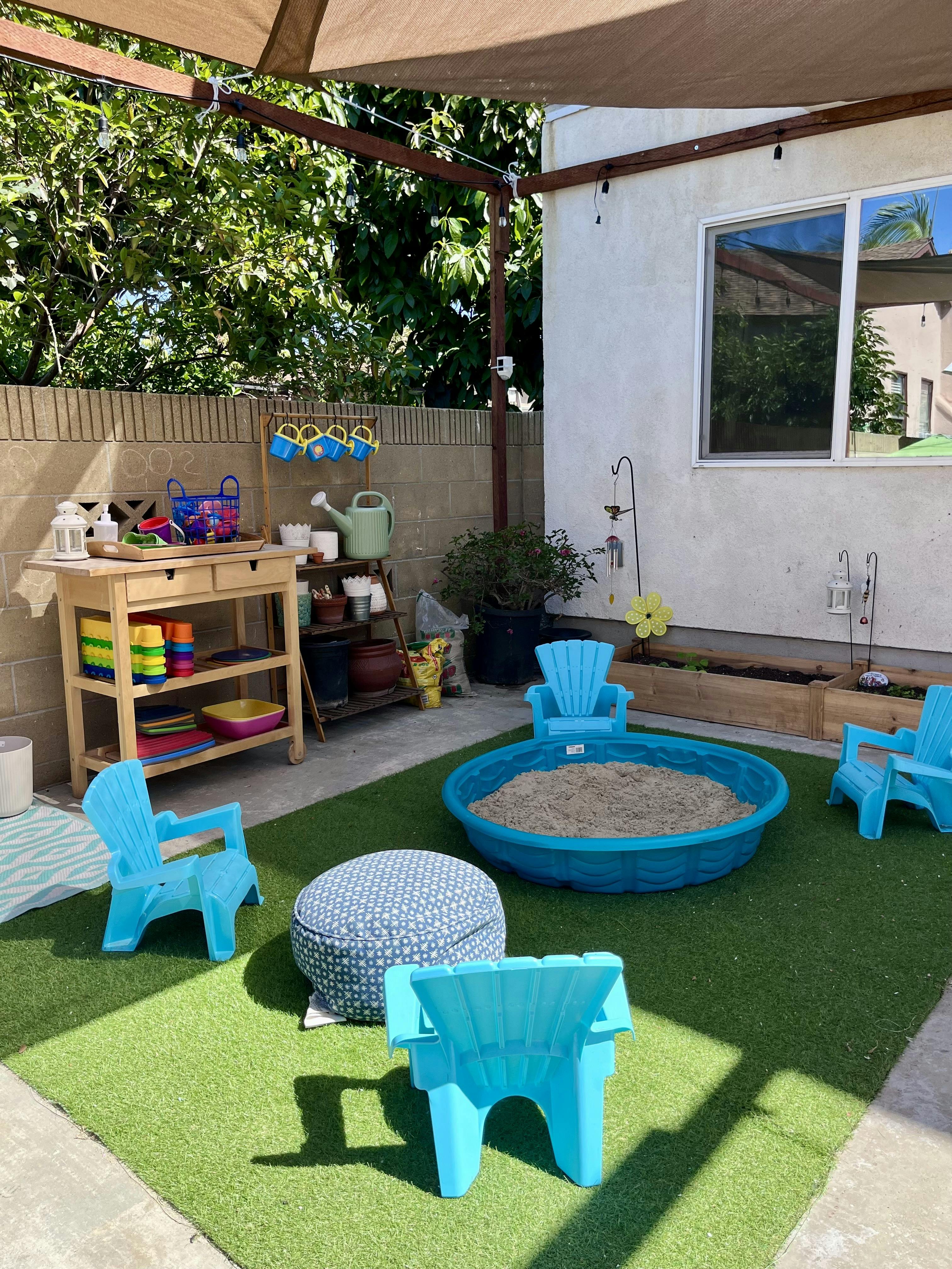 Outdoor play area with sandpit, small chairs, and a wooden table