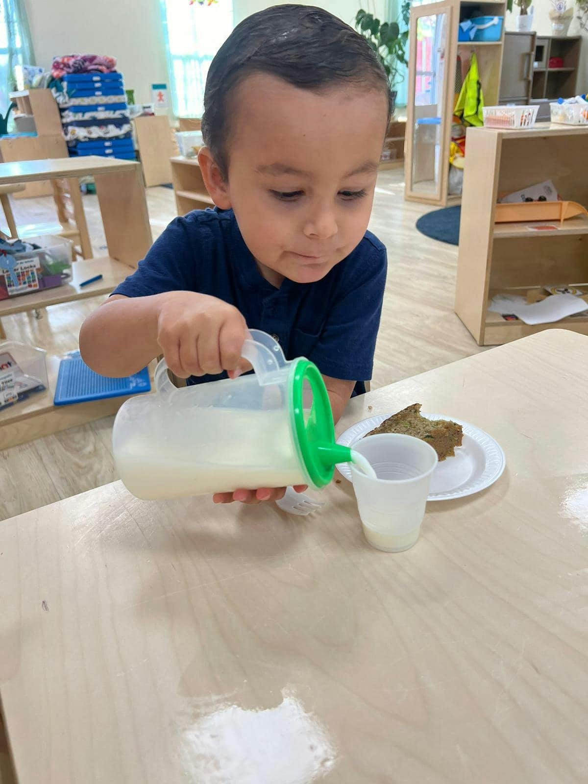 Child pouring liquid from a pitcher into a cup at a table