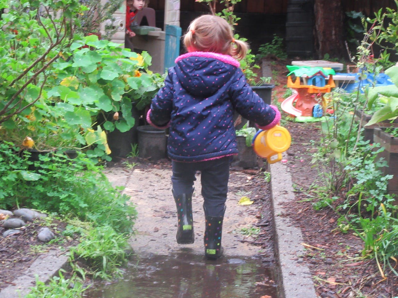 Child in boots walking on a wet path with a watering can