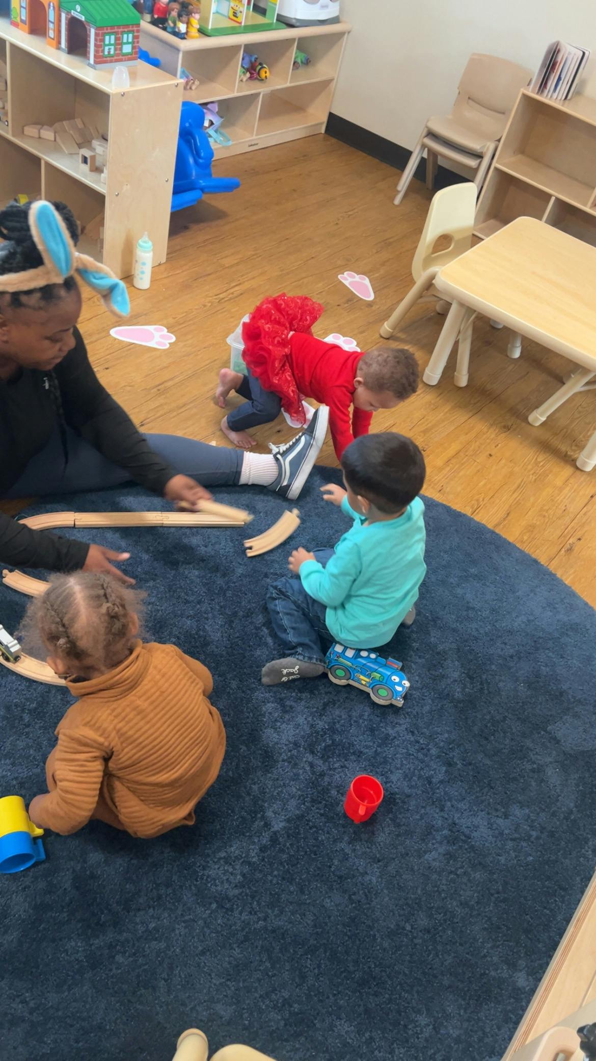Adult and children playing with wooden train tracks on a blue rug