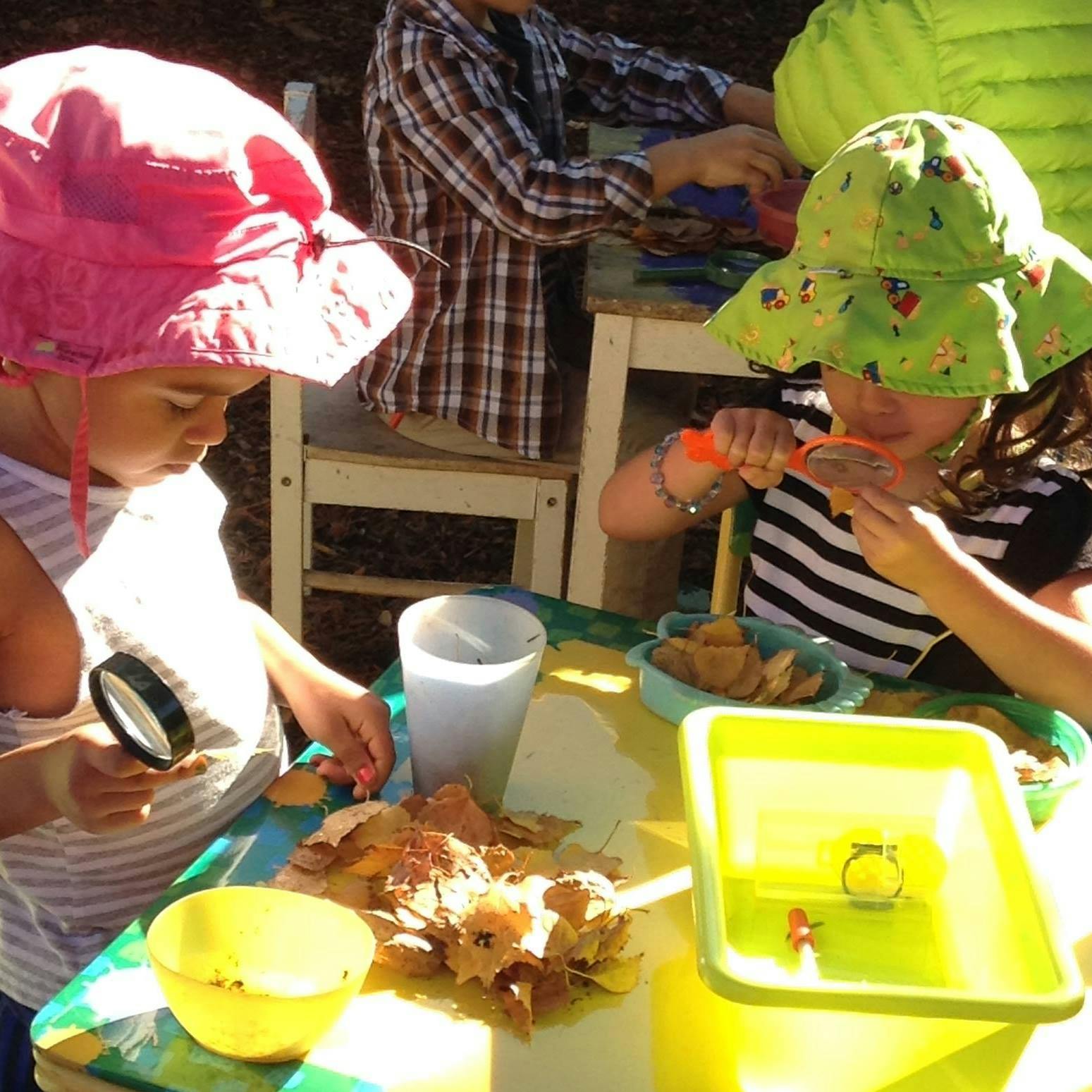 Two children at a table, one holding a magnifying glass, the other using a tool