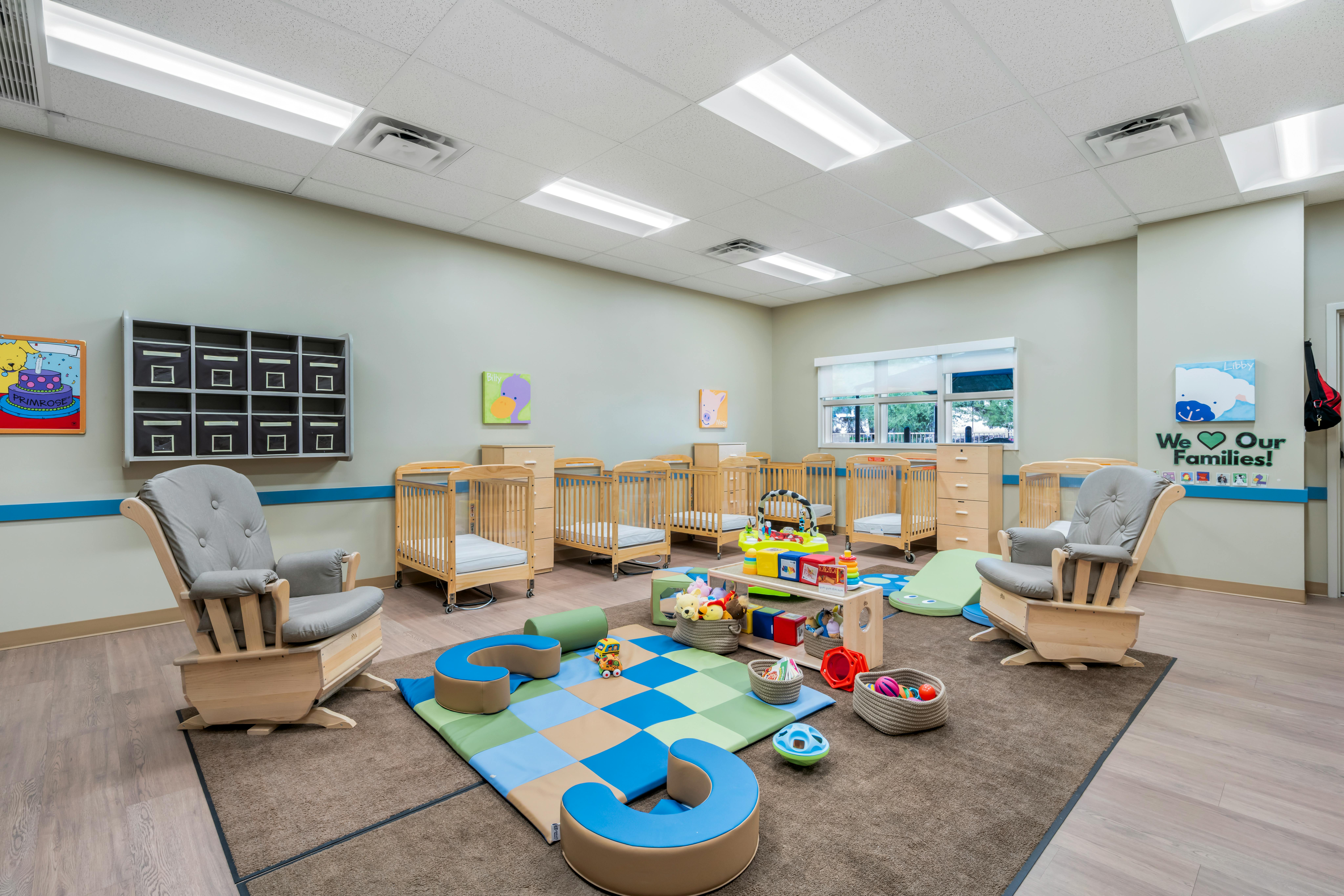 Classroom with multiple cribs, a play mat, toys, and rocking chairs
