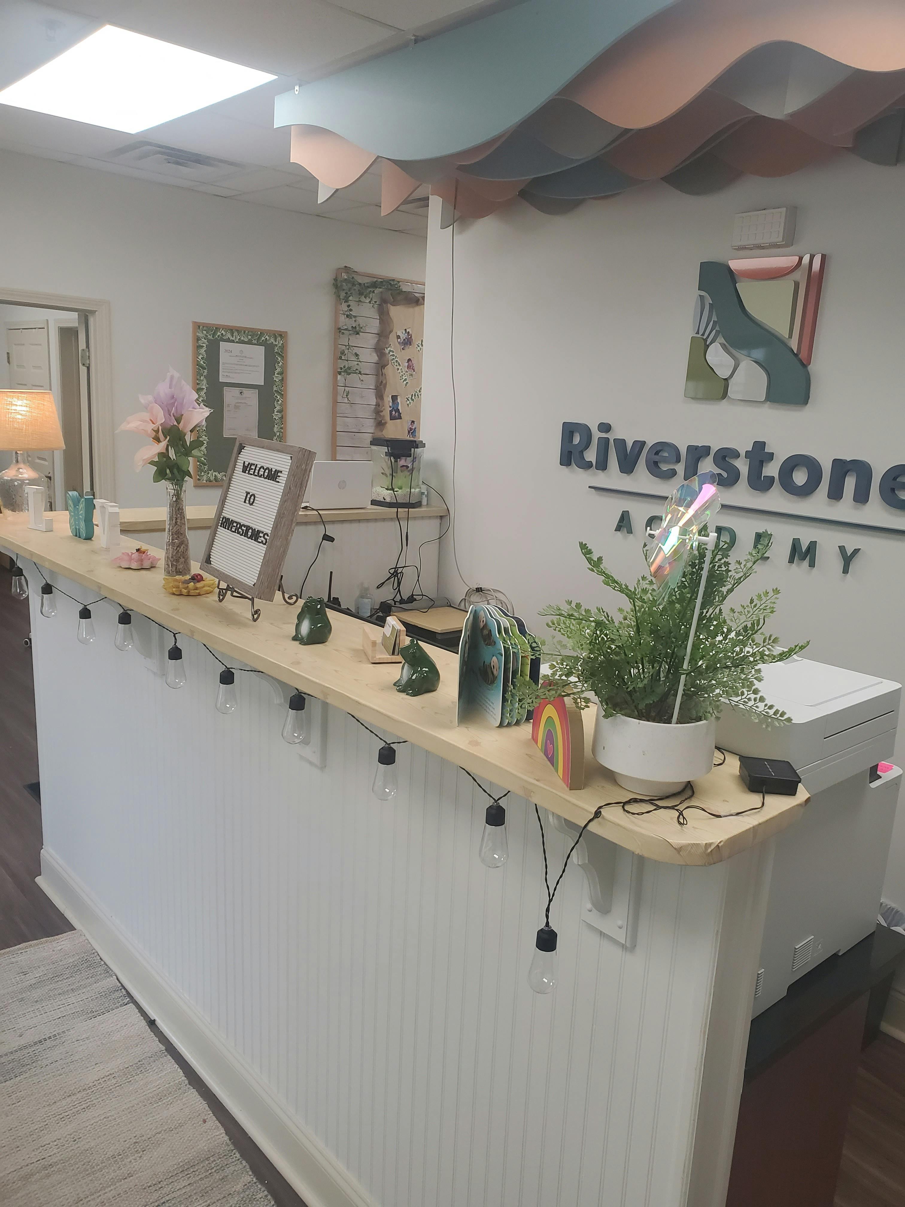 Decorative wall with Riverstone Academy sign, shelves, and various items