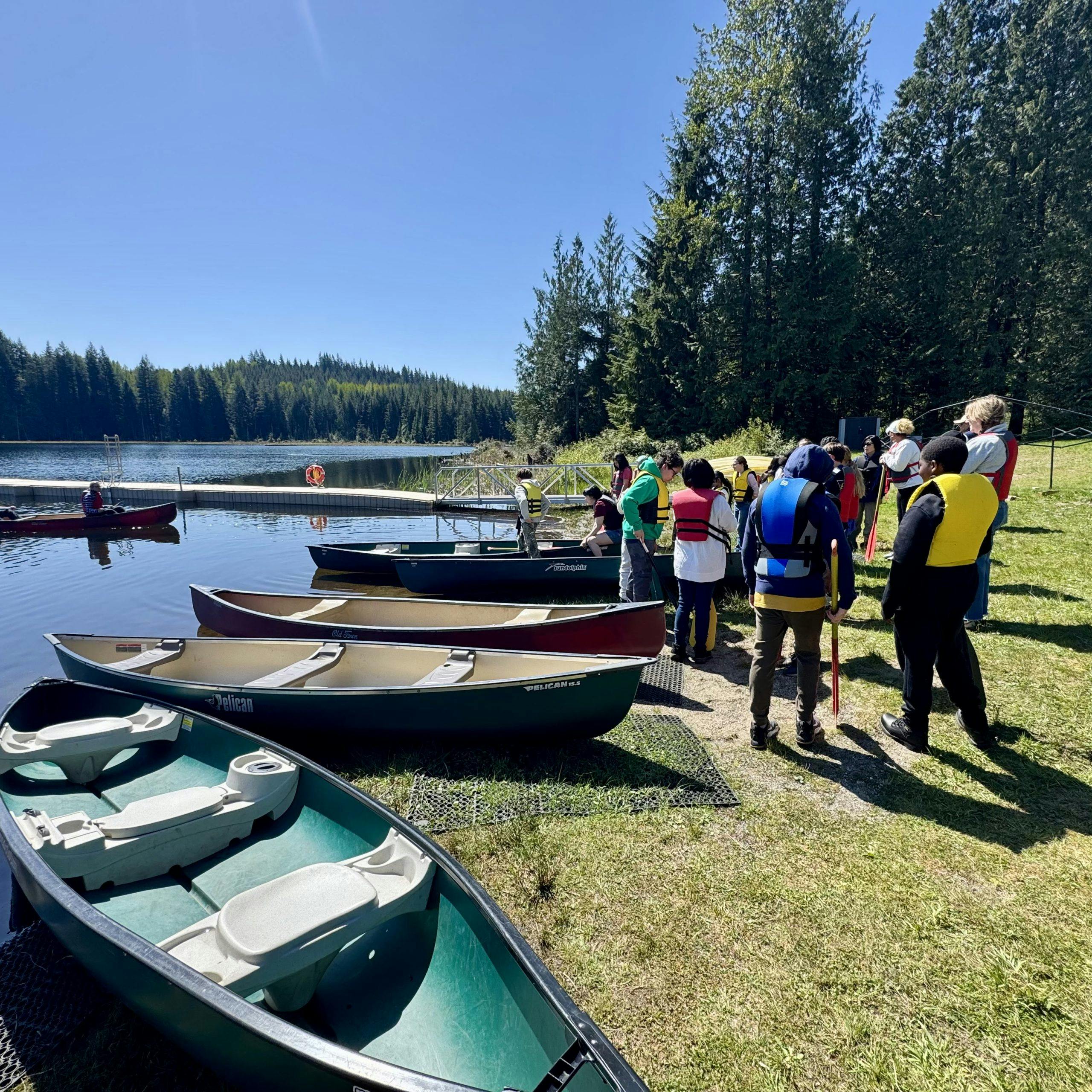 People in life vests by canoes on a lake shore