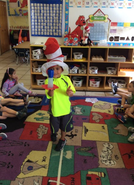 Child in a tall red and white striped hat holding a toy rocket in a classroom