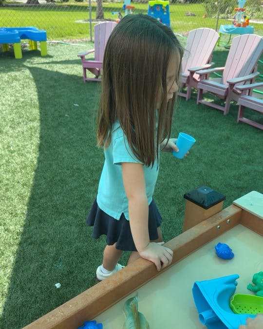 Child standing at a water play table outdoors