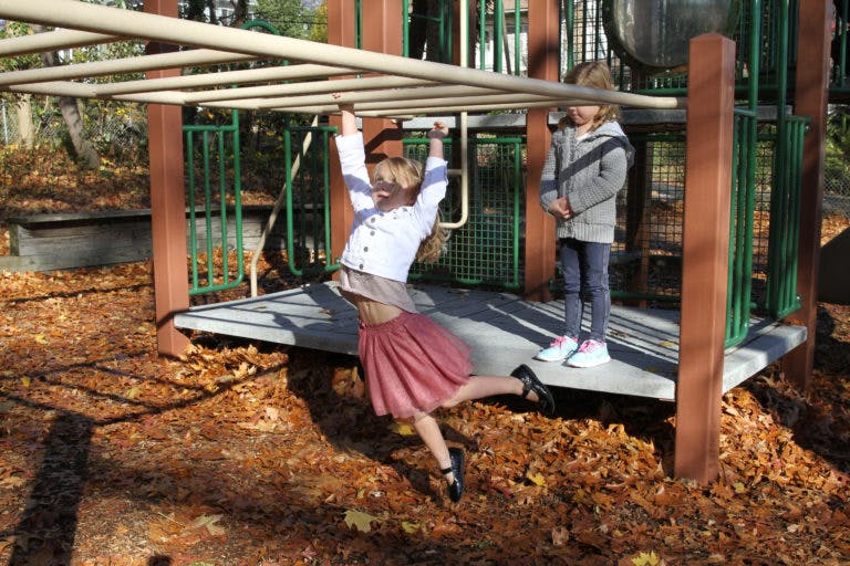 Child on monkey bars with another child standing on a playground