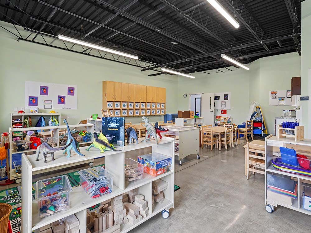 Classroom with shelves of toys, dinosaur figures, and small tables and chairs