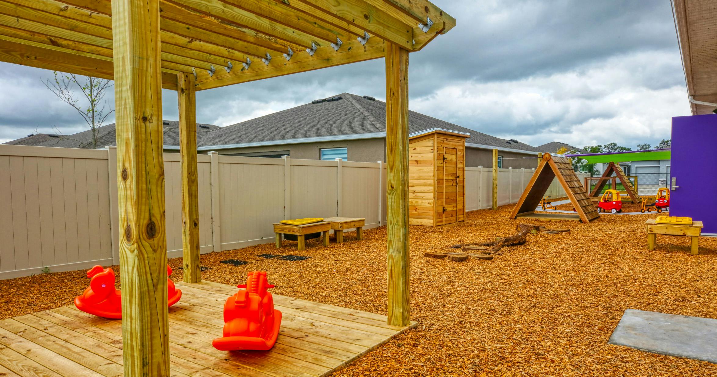 Outdoor children's play area with wooden structures, ride-on toys, and wood chip ground