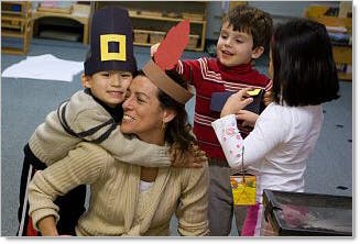 Adult and three children in a classroom, two children wearing hats