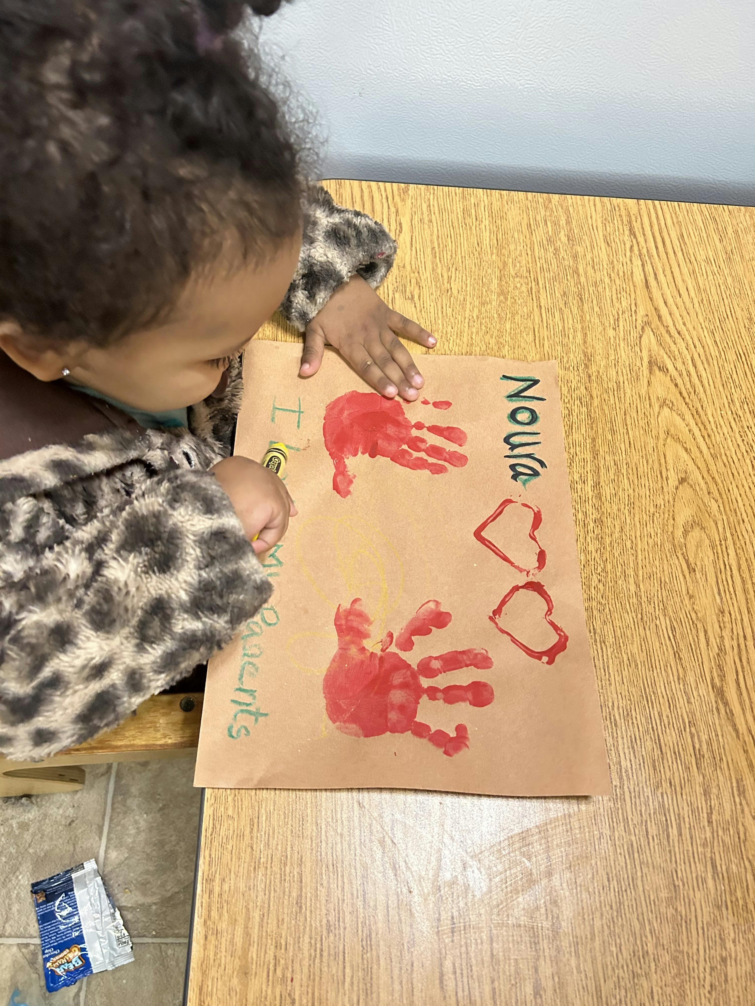 Child looking at a brown paper with two red handprints, red hearts, and text