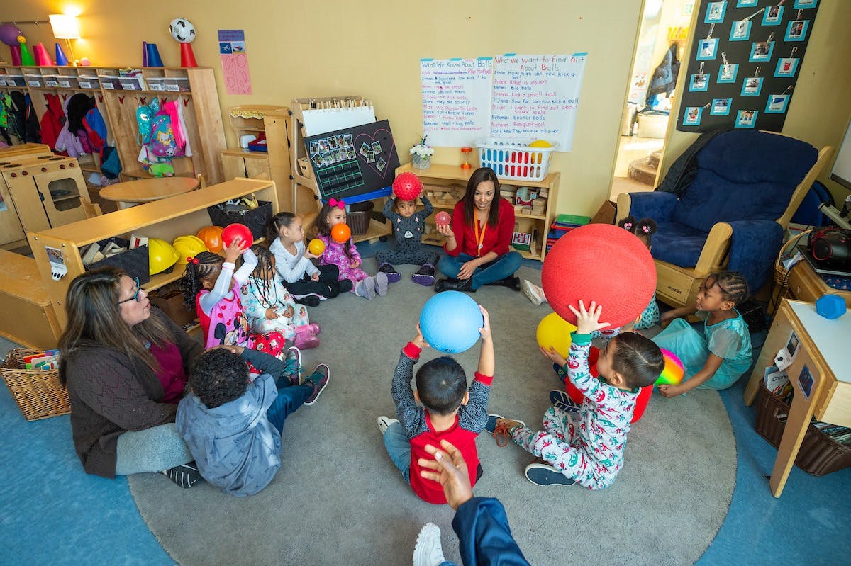 Adults and children sitting in a circle on the floor playing with balls