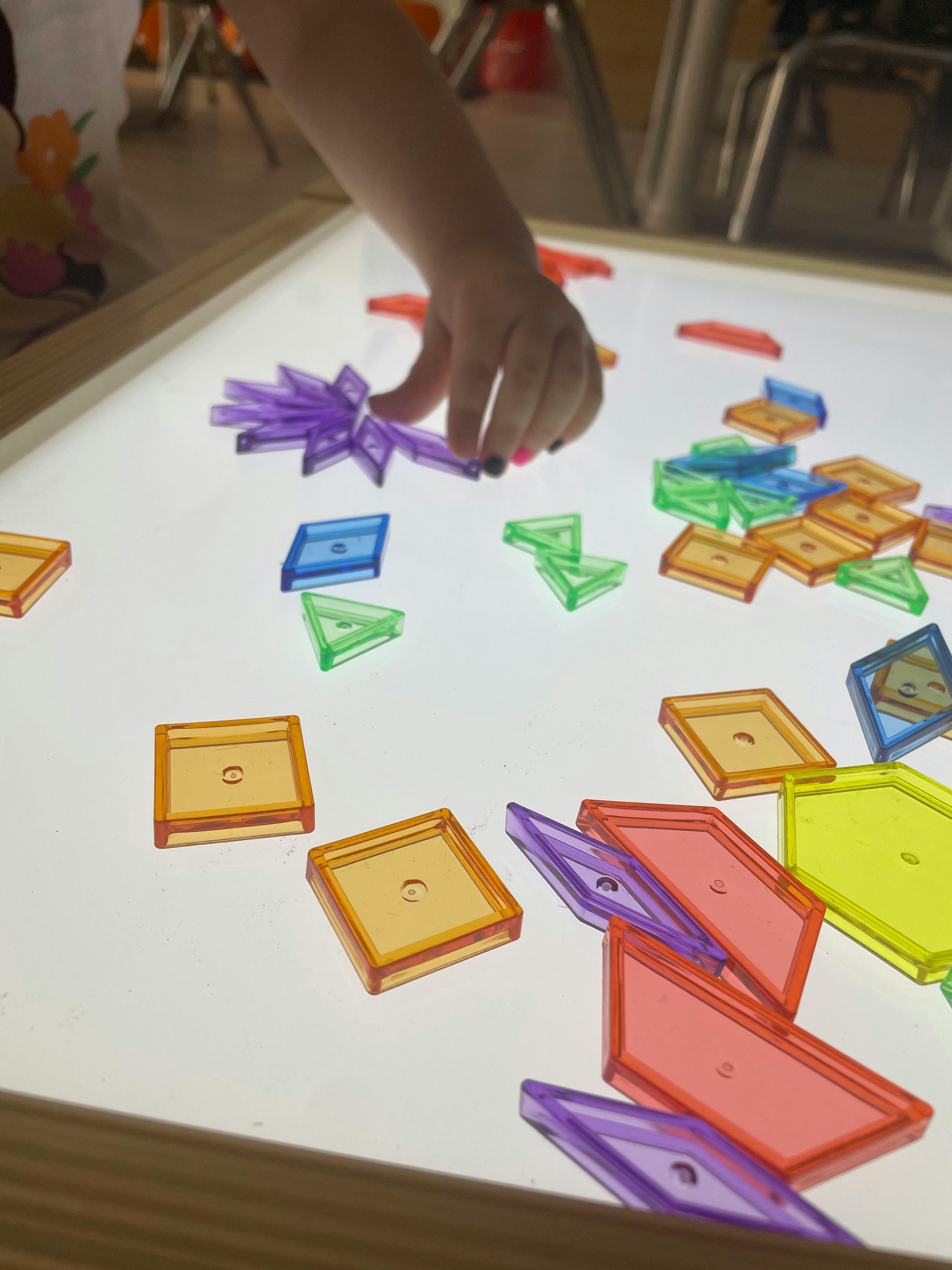 Child's hand arranging colorful translucent blocks on a light-up surface