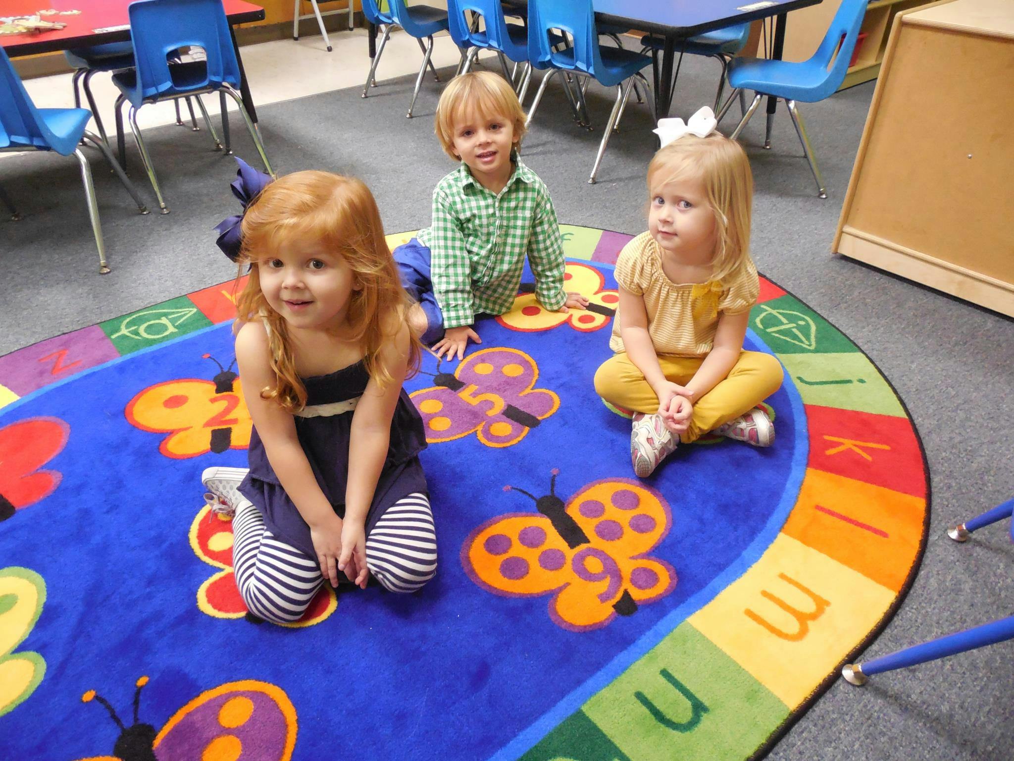 Three children sitting on a colorful rug with butterfly designs