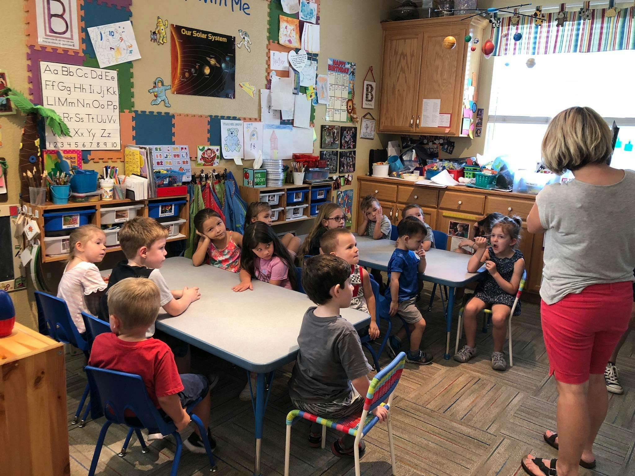 Adult standing in a classroom with children seated at tables