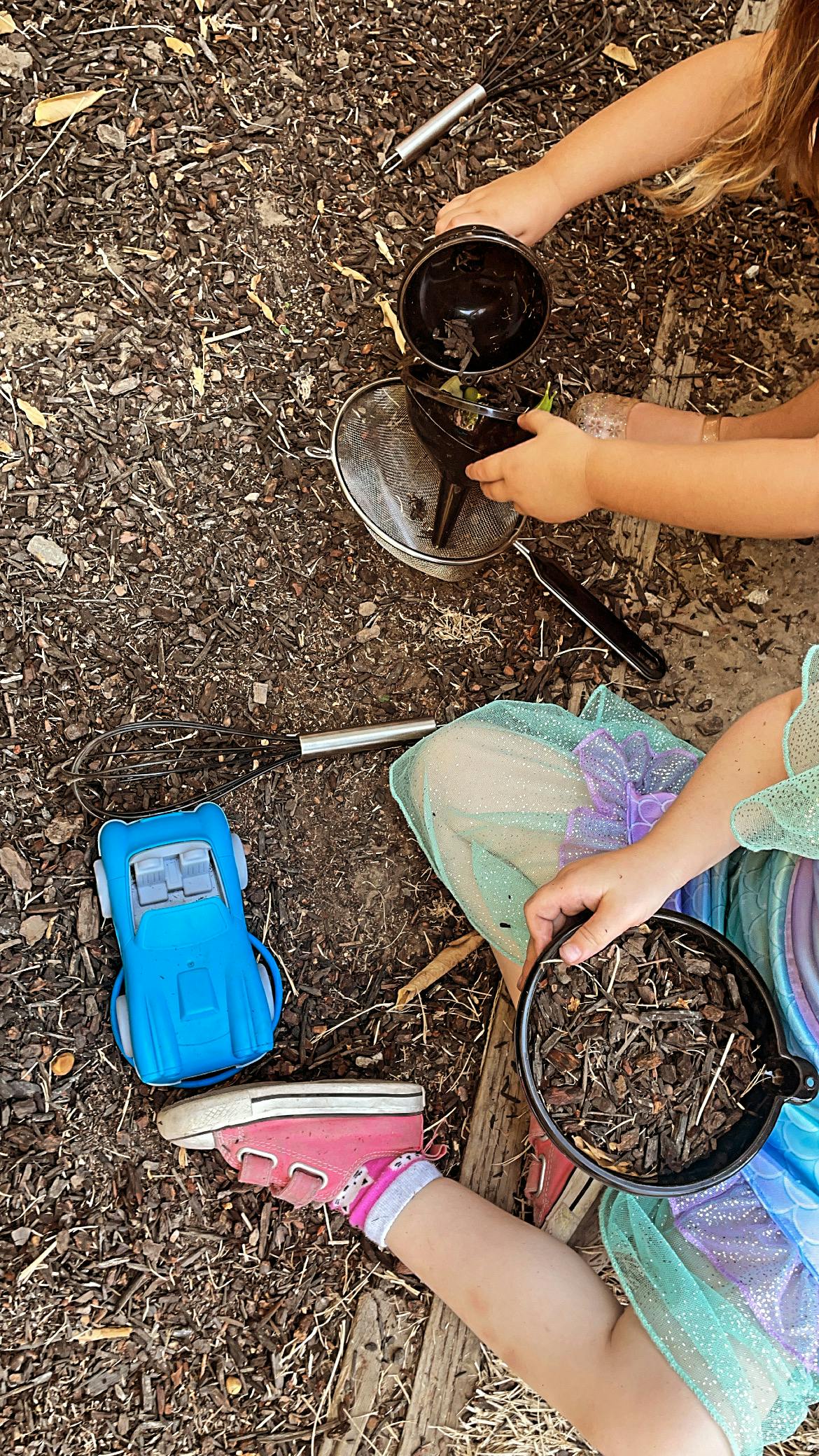 Child playing with dirt and kitchen utensils, a blue toy car nearby