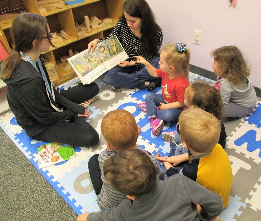 Adult reading a book to a group of children in a classroom