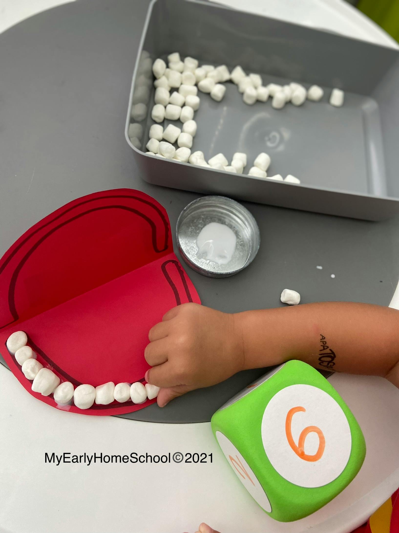 Child's hand placing marshmallows on a red paper mouth with a green die showing number 6