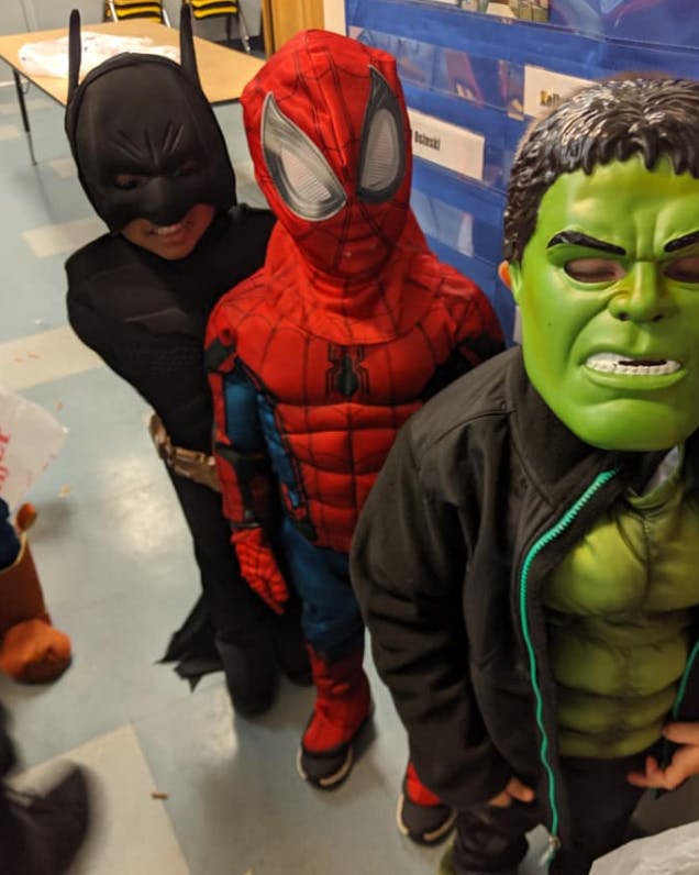 Three children in superhero costumes, including Batman, Spider-Man, and Hulk