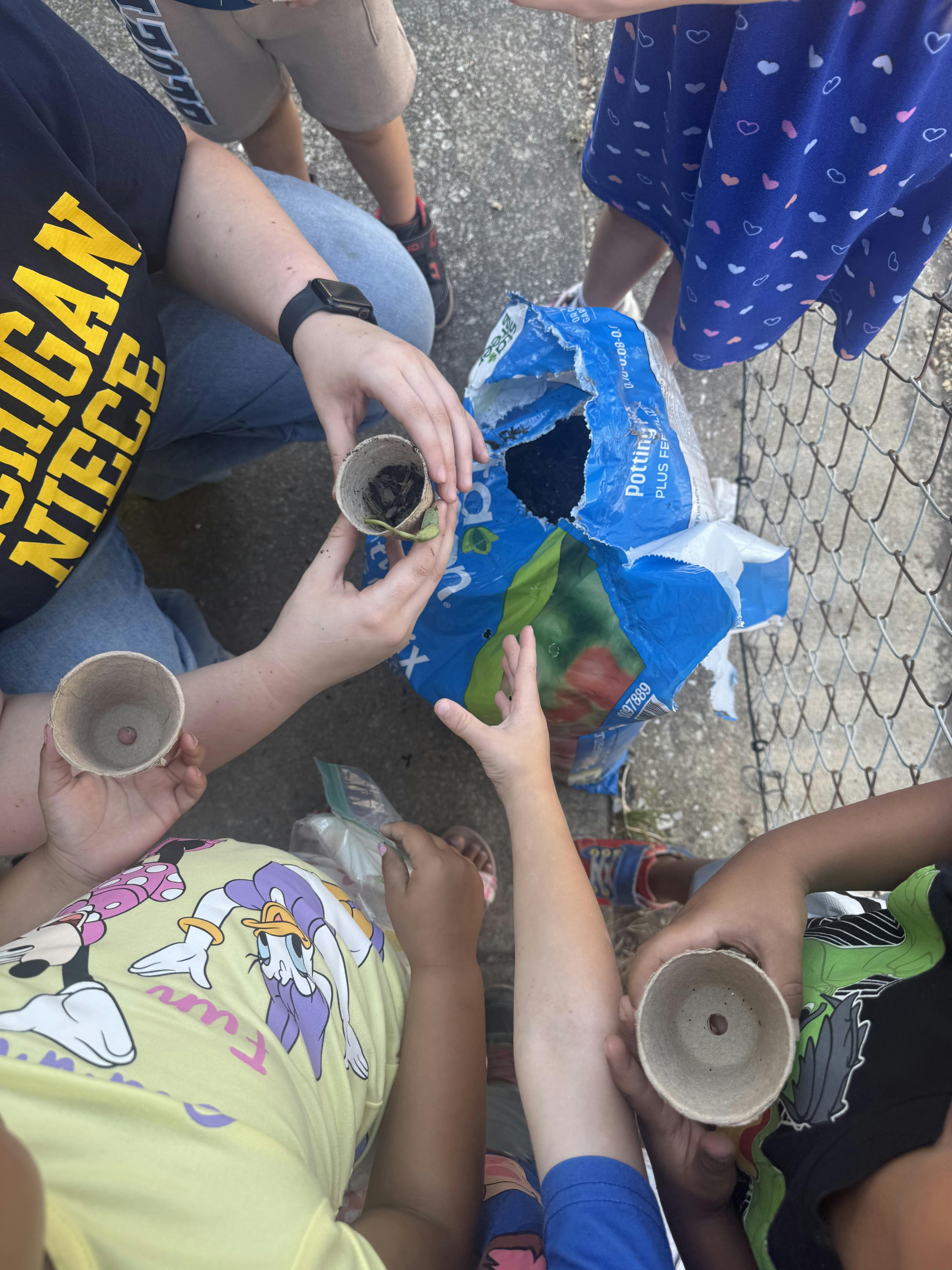 People holding small planting pots near a bag of potting soil
