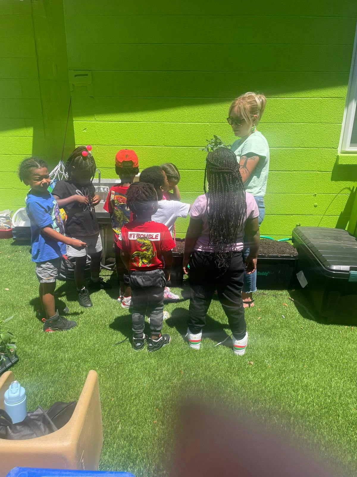 Adult and children gathered around a planter in a grassy area