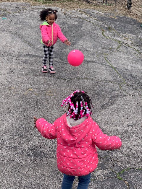 Two children playing with a pink ball outdoors