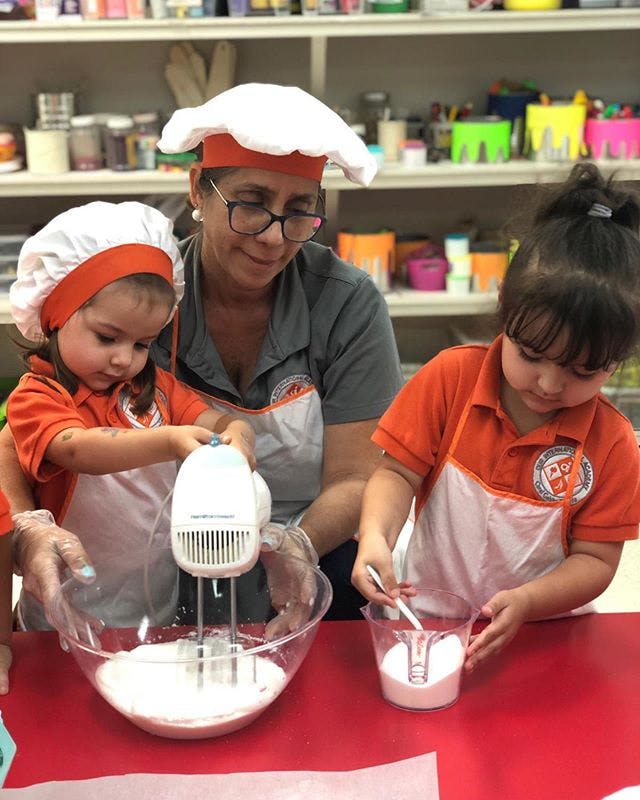 Adult and two children in chef hats and aprons mixing ingredients