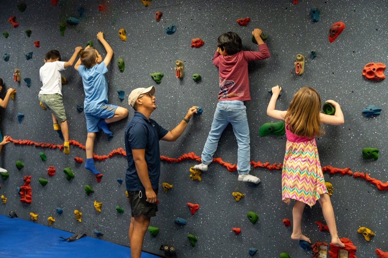 Adult and multiple children climbing on an indoor rock wall