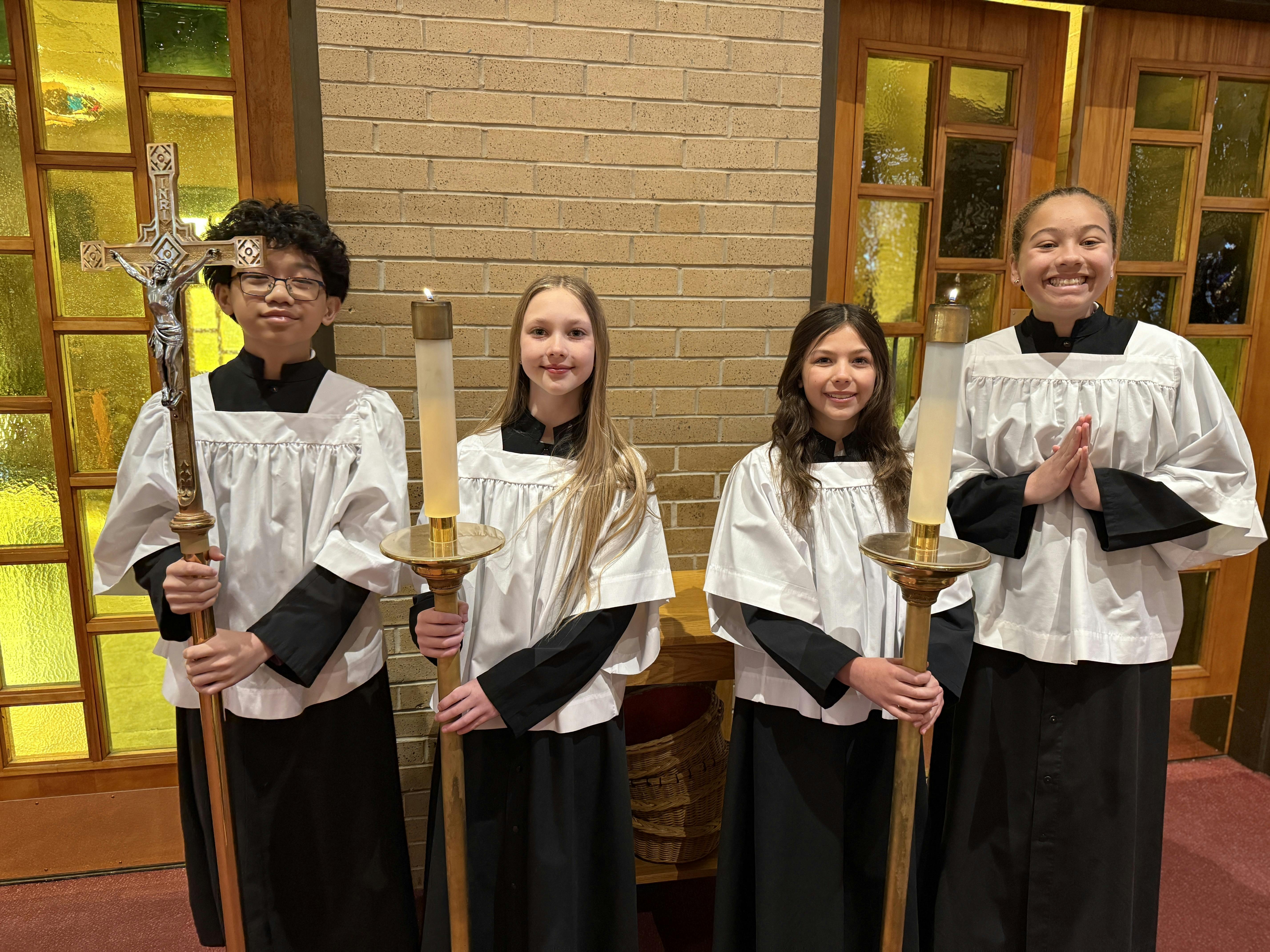 Four children in robes holding a cross and candles