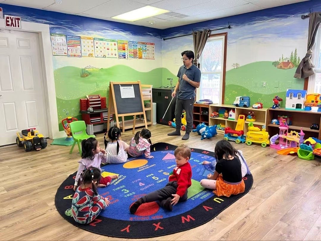 Teacher pointing to a chart for children sitting on a rug in a playroom