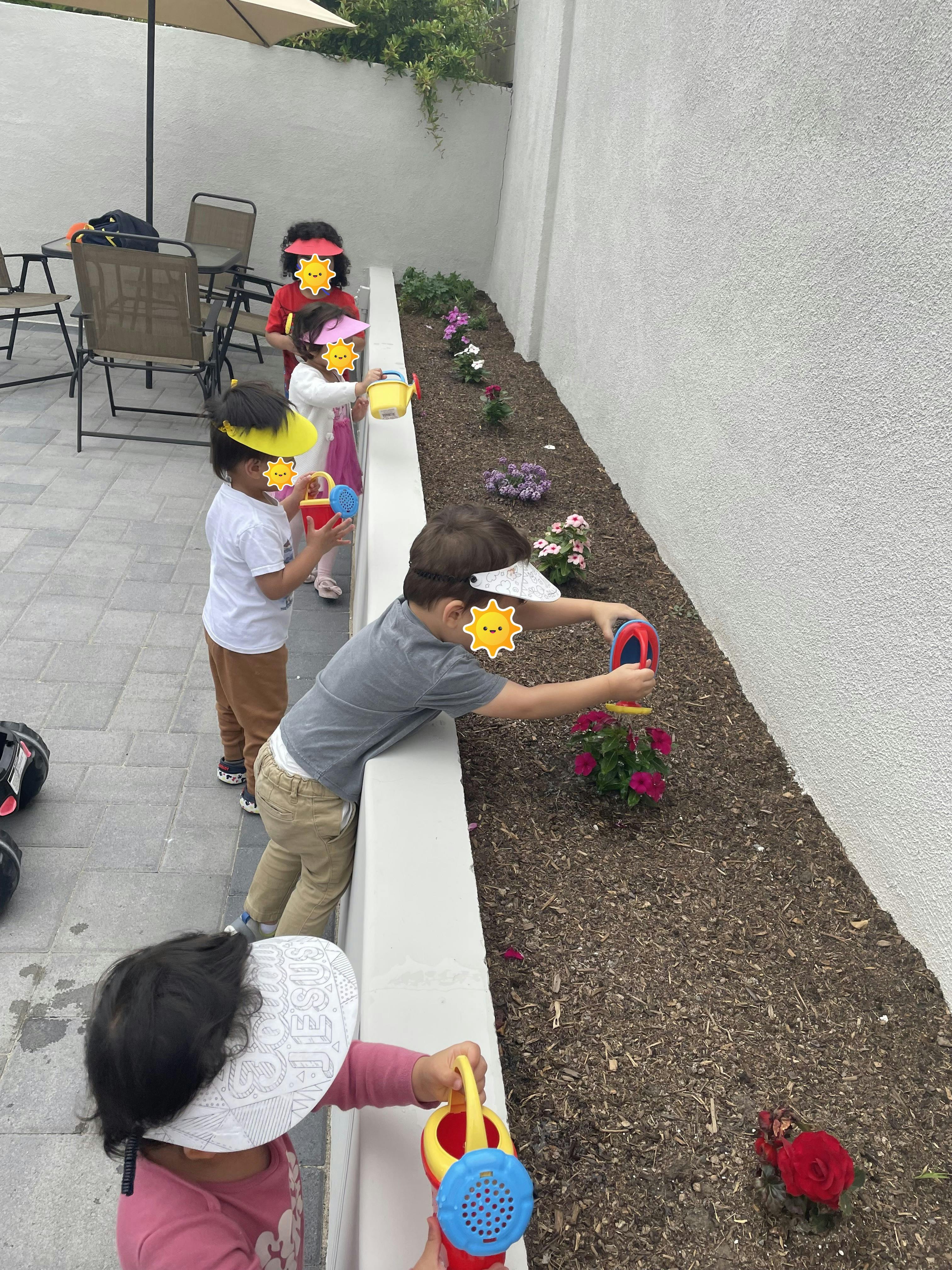 Children watering plants in a garden bed with small watering cans