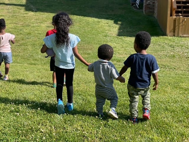 Three children holding hands and walking on grass