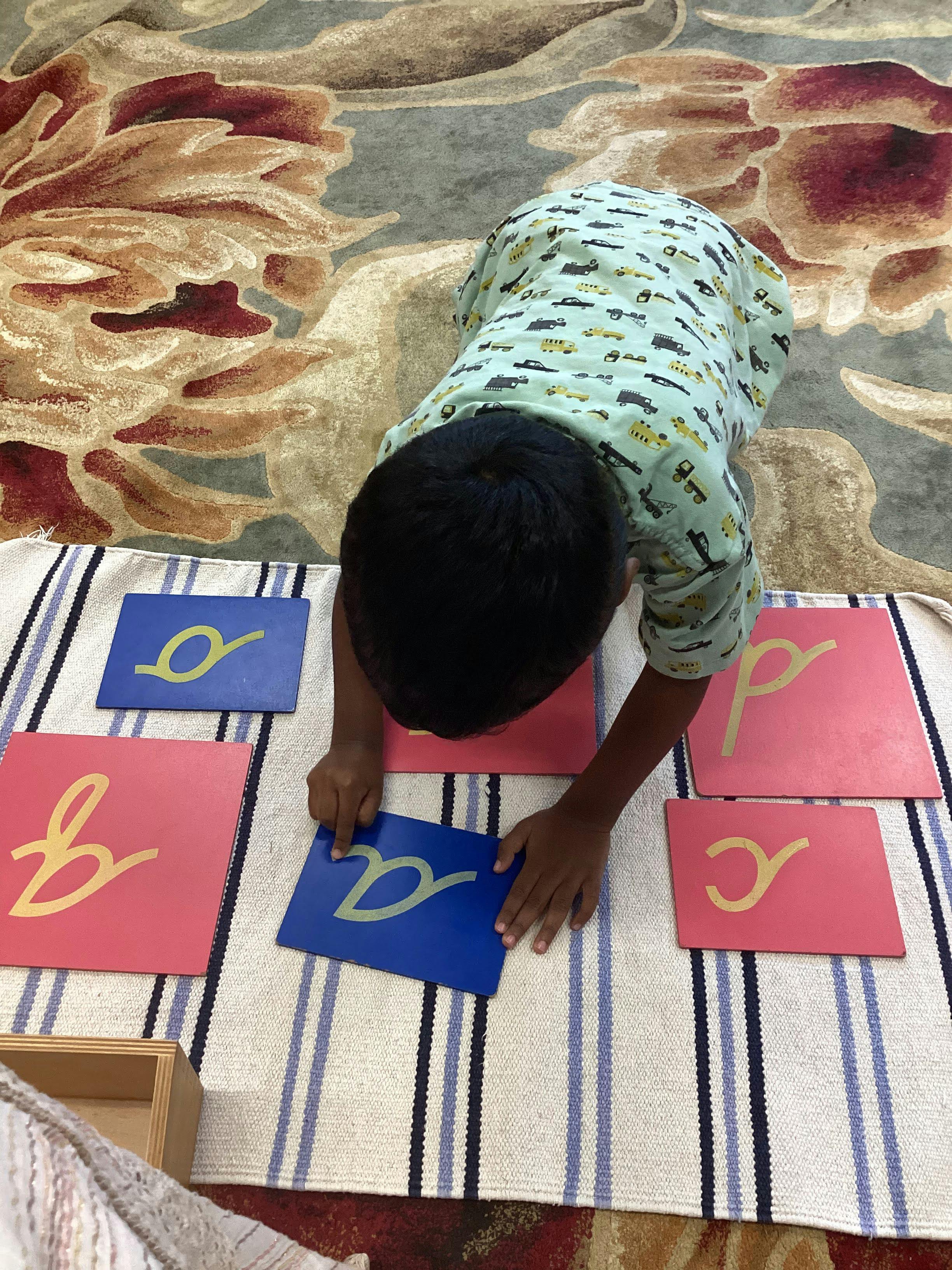 Child on floor tracing a letter on a blue card with other letter cards around