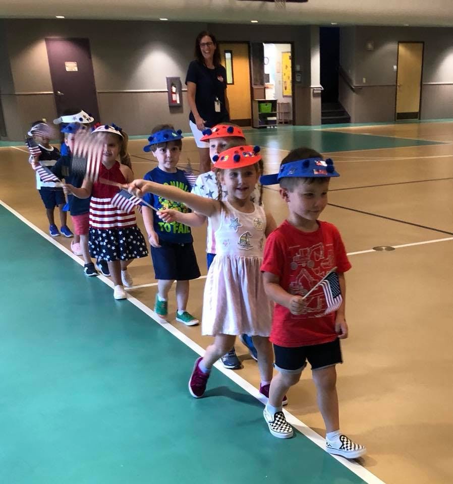 Children in a line holding small flags, with an adult in the background