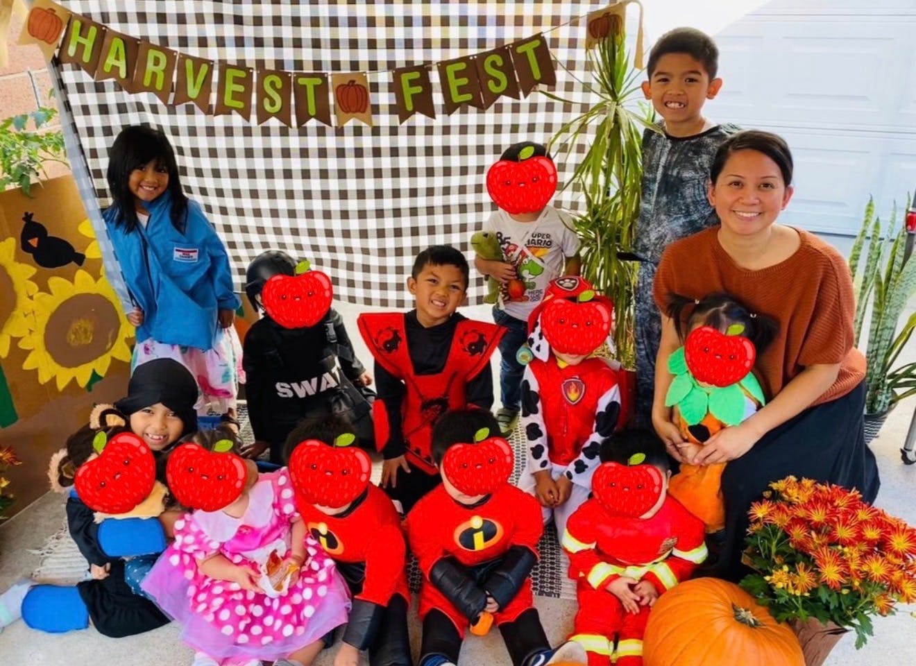 Group of children and a person posing in front of a Harvest Fest banner