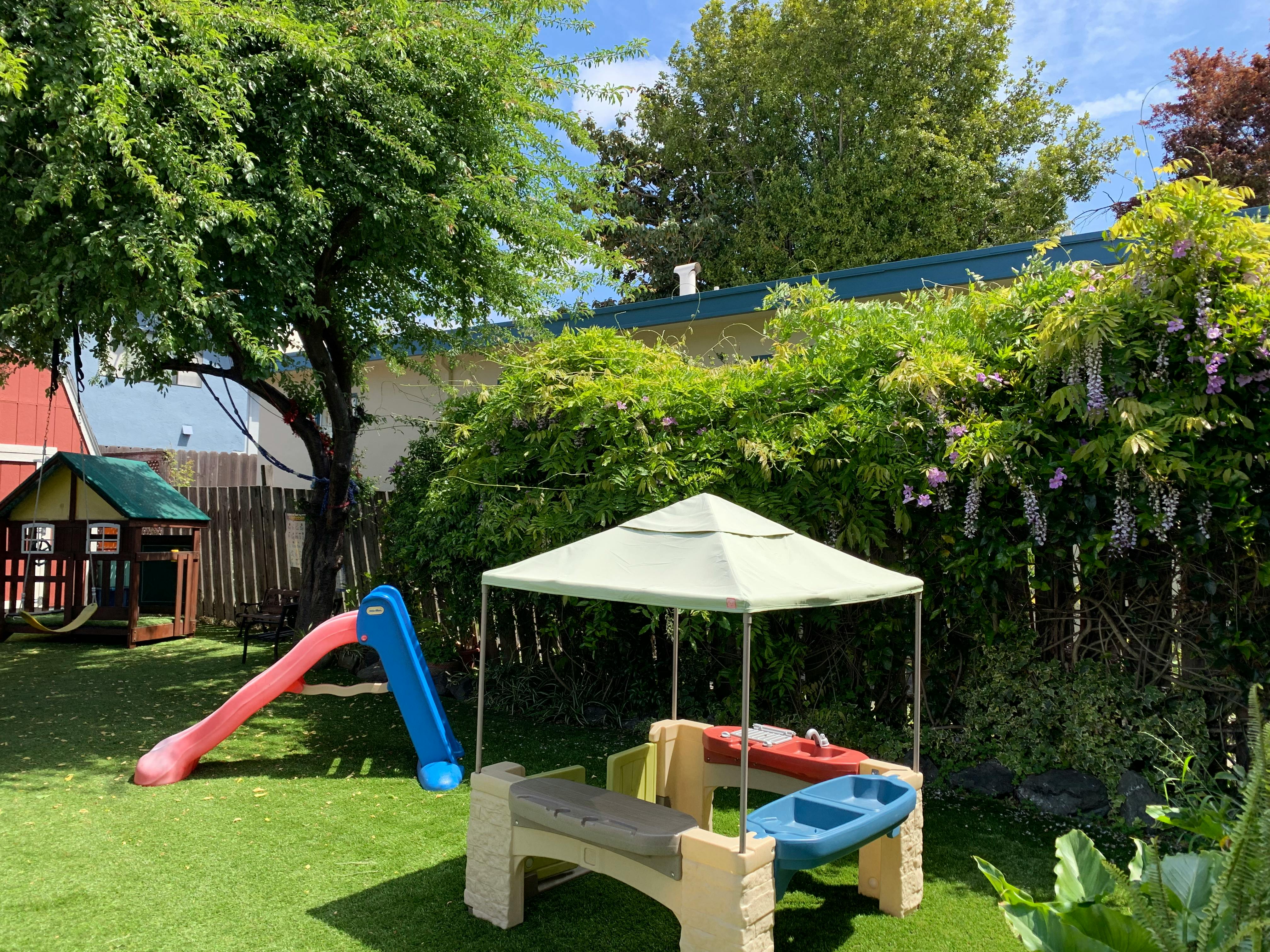 Playground with a slide, playhouse, and canopy over a table and bench