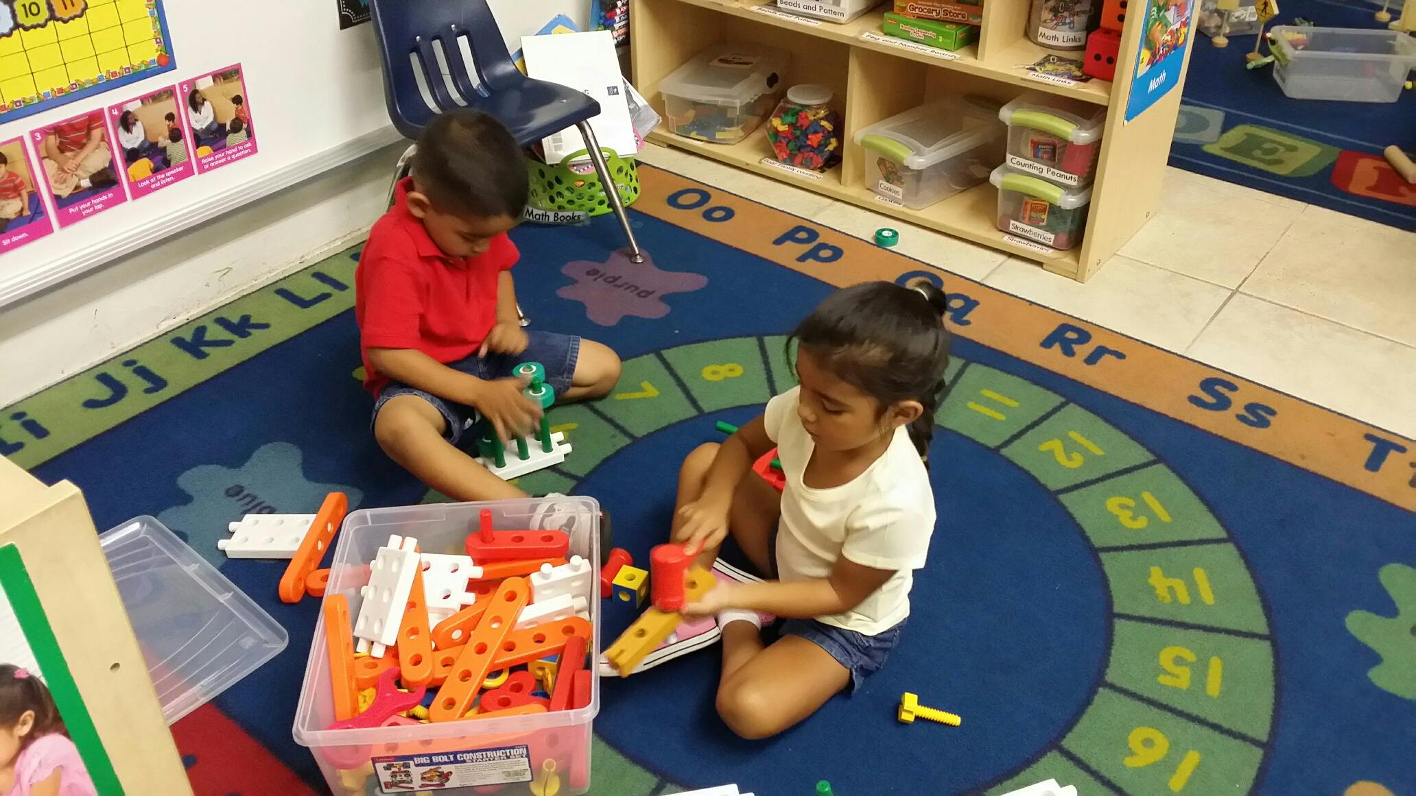 Two children playing with building toys on a rug in a classroom